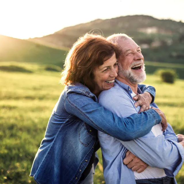 Happy senior couple outside in spring nature, hugging at sunset. Side view.