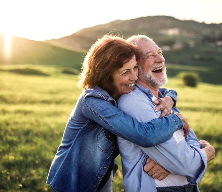 Happy senior couple outside in spring nature, hugging at sunset. Side view.