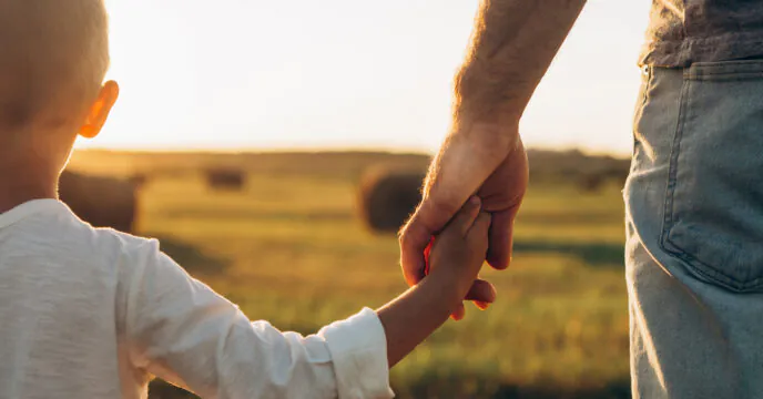 Fathers and his son holding hands at sunset field